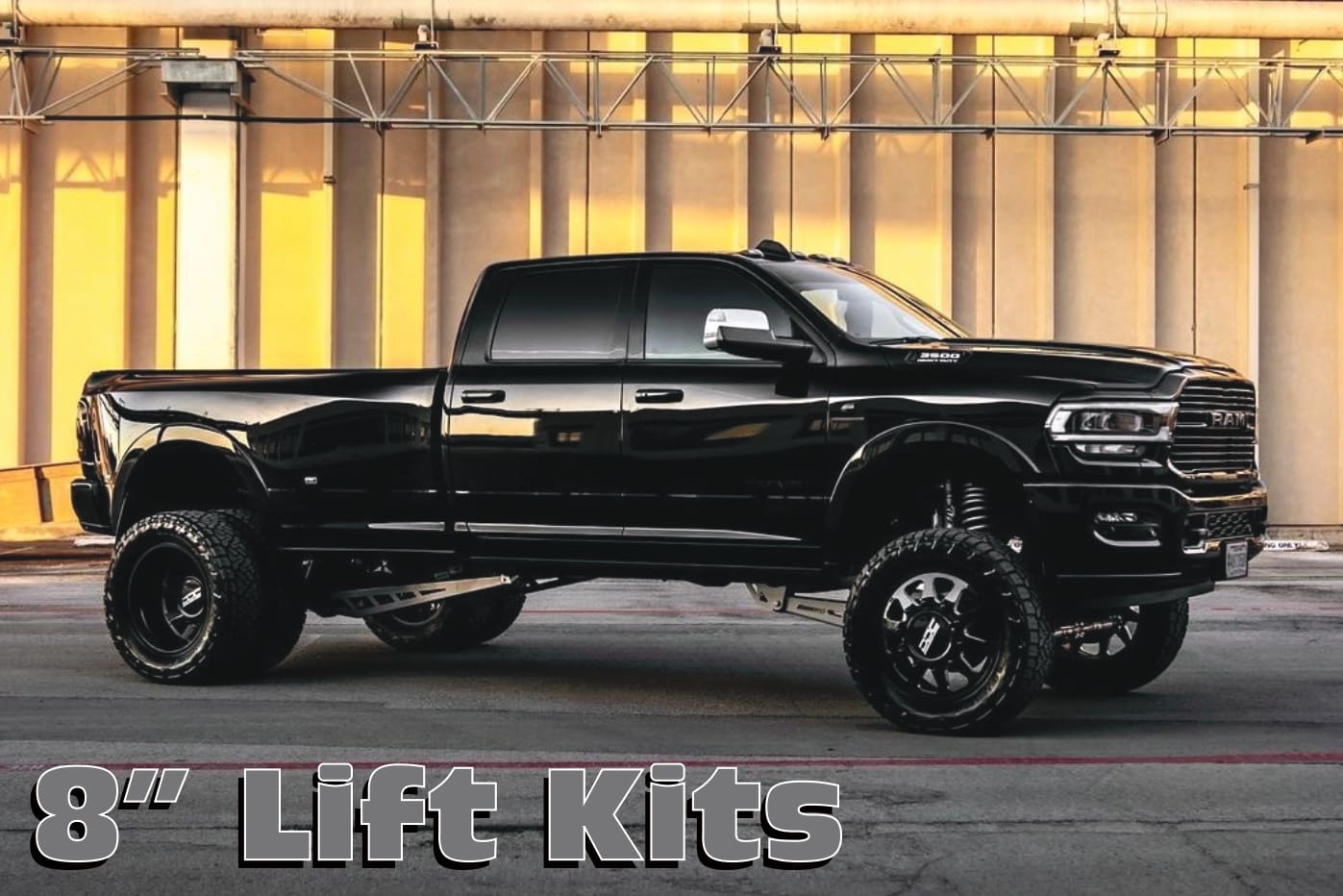 A black truck with huge tires parked in front of a building.