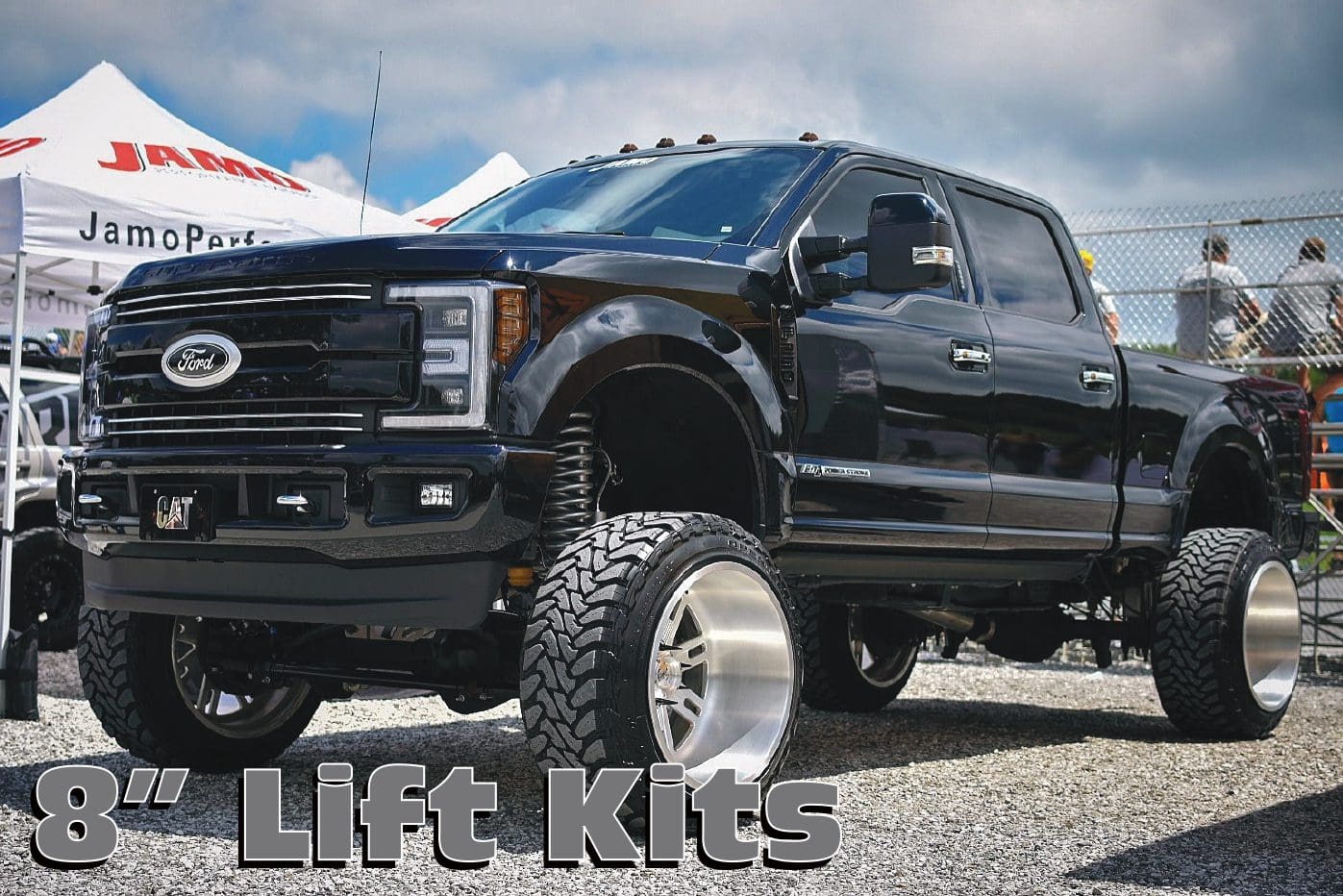 A black truck with huge tires is parked in the dirt.